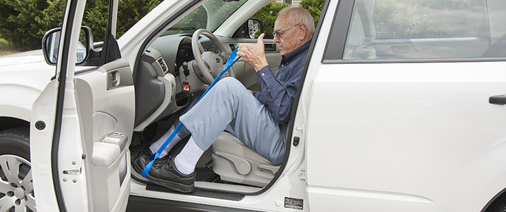 Senior man using leg-lifting strap tool to get into car Senior man using leg-lifting strap tool to get into car